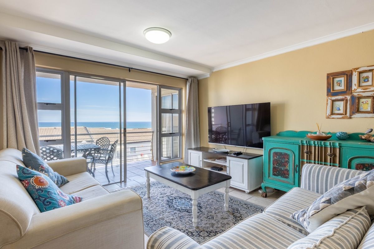 A bright living room featuring large sliding glass doors that open onto a balcony with ocean views and tiled flooring throughout.