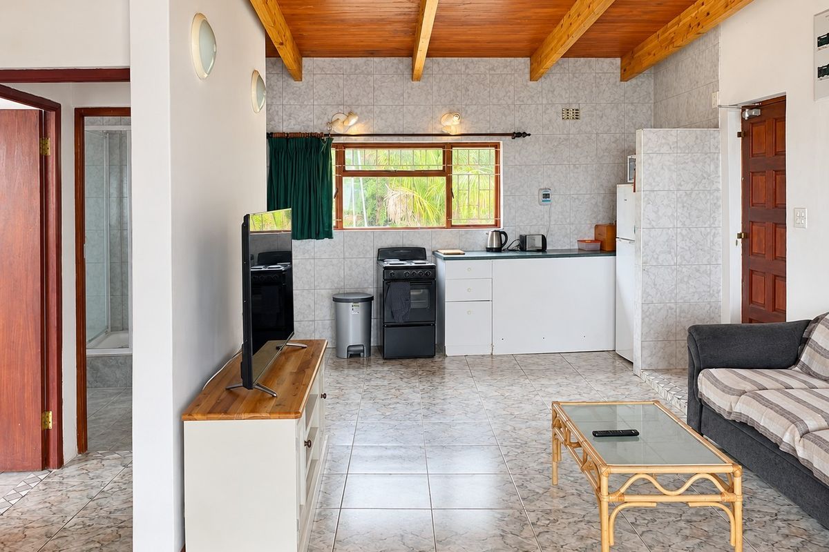 Open-plan living area featuring exposed timber ceiling beams, tiled flooring, and a functional kitchen space with built-in cabinetry and a freestanding stove.