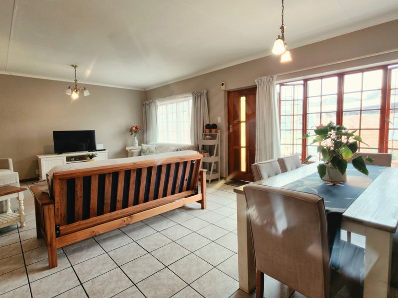 Spacious open-plan living and dining area featuring neutral wall tones, tiled flooring, and large timber-framed windows providing ample natural light.