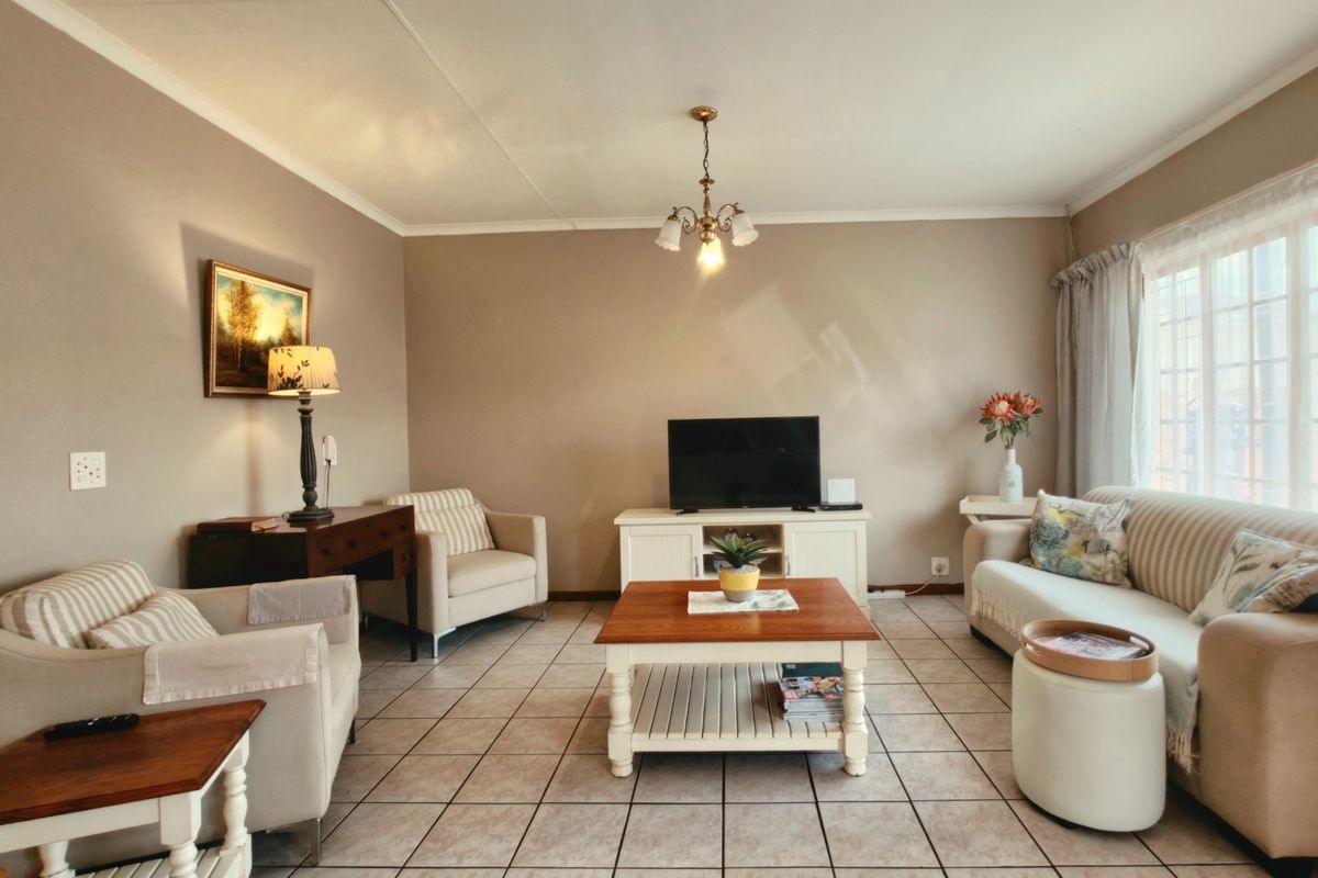 A comfortable living room featuring neutral wall tones, tiled flooring, and a large window that provides ample natural light.