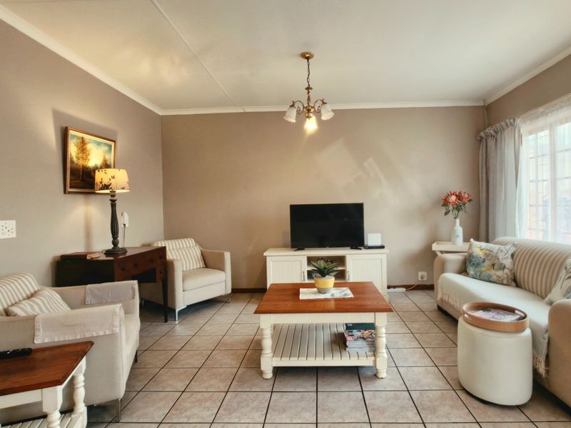 A comfortable living room featuring neutral wall tones, tiled flooring, and a large window that provides ample natural light.