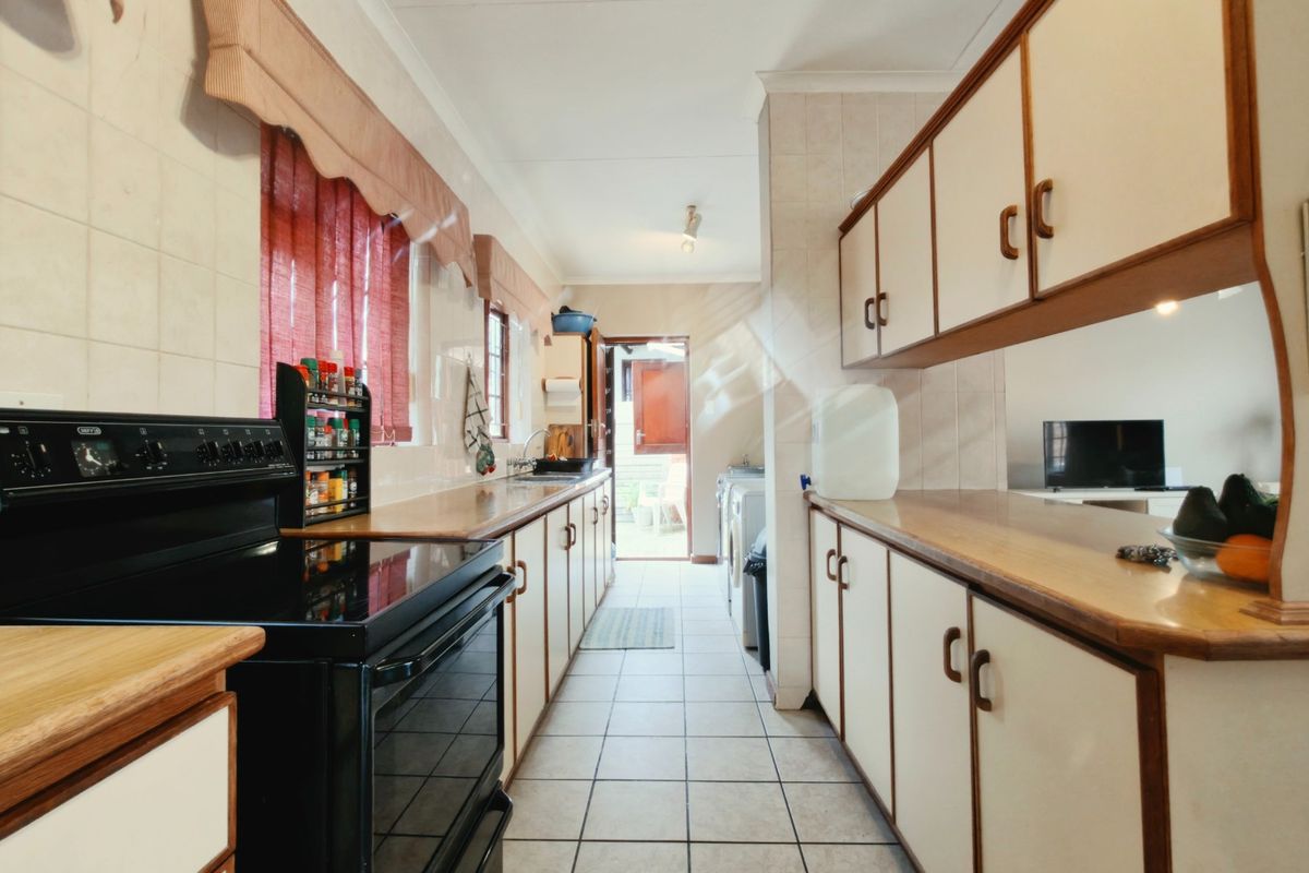 A functional galley-style kitchen featuring ample built-in cabinetry, laminate countertops, tiled flooring, and a freestanding oven, leading directly to an exterior door.