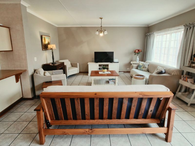 An open-plan living area featuring tiled flooring, a breakfast bar, and natural light through a window with mullions.