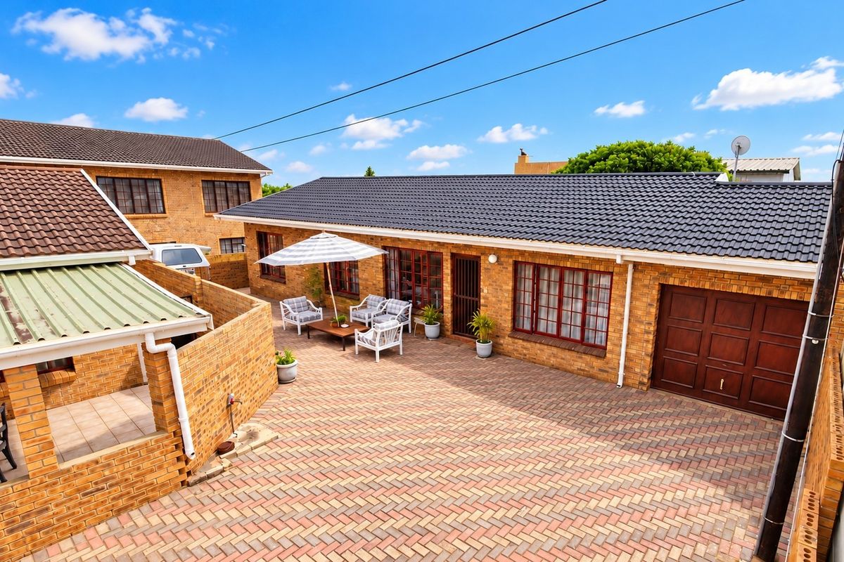 A well-maintained rear courtyard featuring extensive brick paving, a tiled roof structure, and a secure garage entrance.