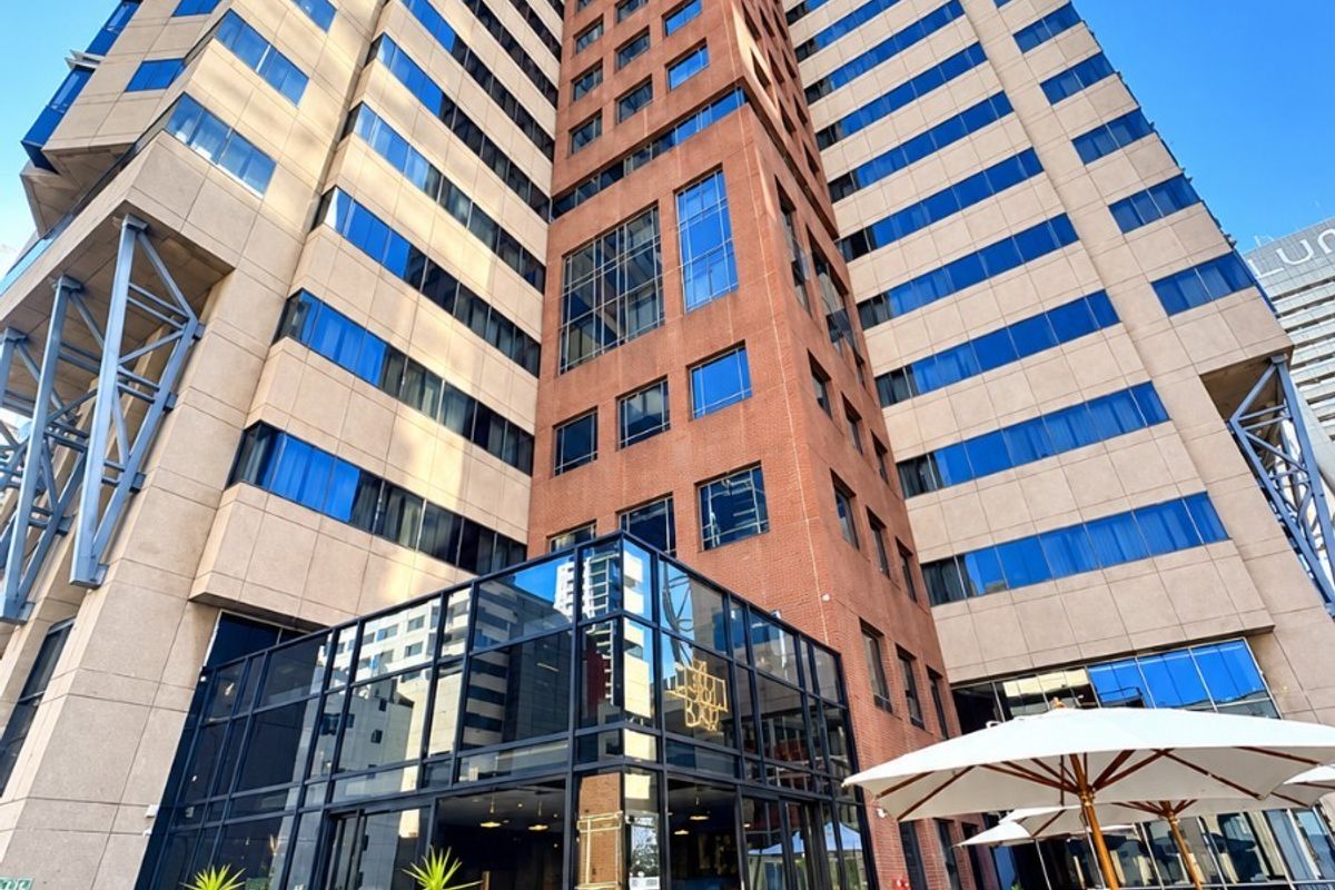A low-angle view of a modern high-rise apartment building featuring a timber deck terrace and extensive glass facade architecture.