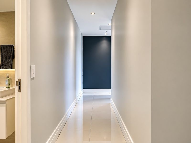 A clean, modern hallway with neutral walls, polished tile flooring, and recessed lighting, leading to a dark accent wall.