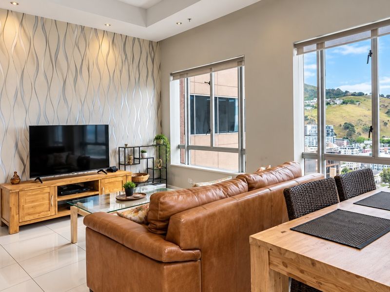 Bright open-plan living and dining area featuring large windows with city views, modern tiled flooring, and a decorative feature wall.