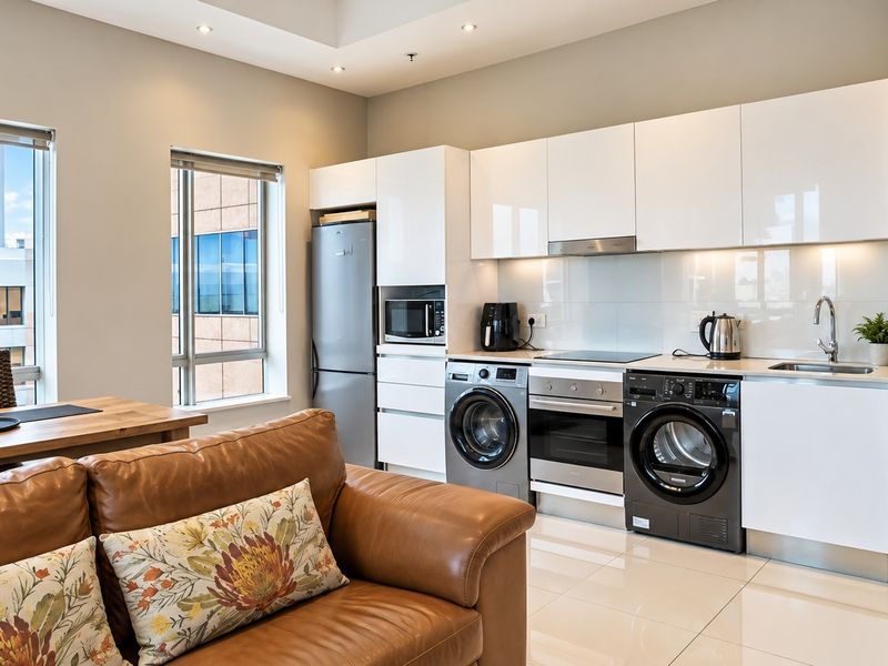 Modern open-plan living area featuring a sleek kitchen with high-gloss cabinetry, integrated appliances, and polished tiled flooring, offering a bright and contemporary living space.