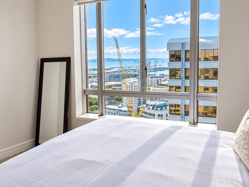 A bright bedroom featuring large floor-to-ceiling windows that offer expansive city and harbour views.