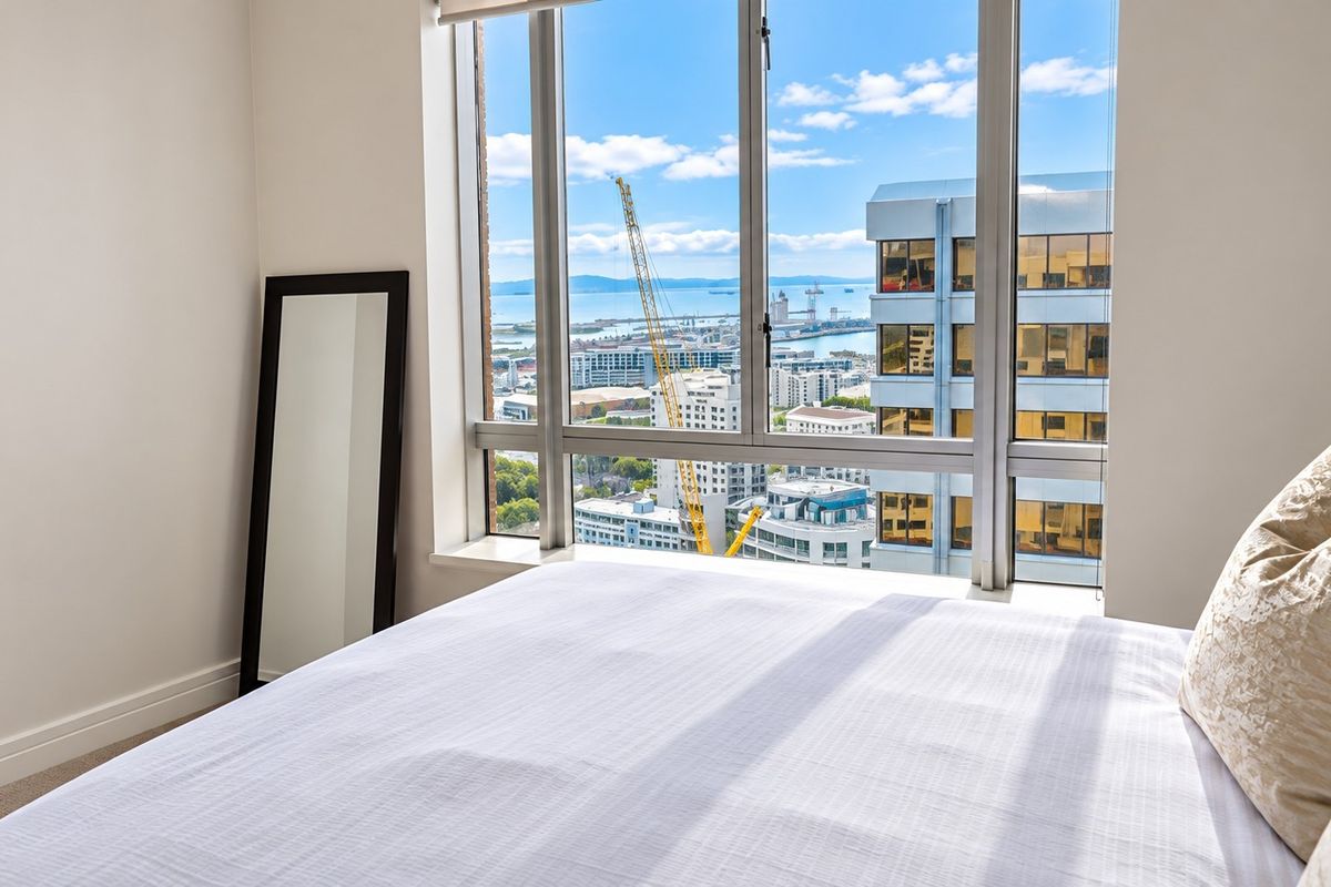 A bright bedroom featuring large floor-to-ceiling windows that offer expansive city and harbour views.