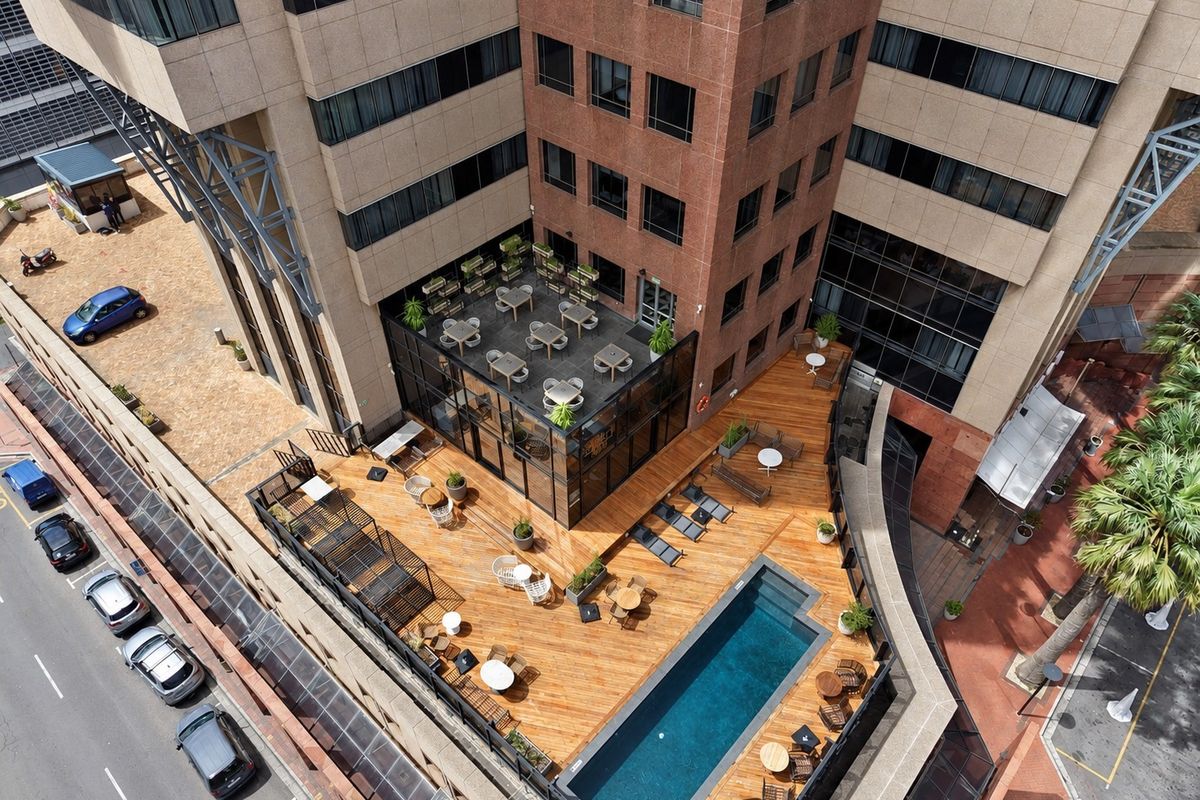 Aerial view of a modern apartment building featuring a rooftop terrace with a swimming pool, wooden decking, and glass-enclosed common areas.