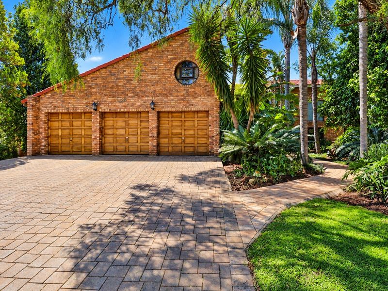 A well-maintained front exterior featuring a triple garage with wooden doors, a brick facade, and a neatly paved driveway surrounded by lush garden landscaping.
