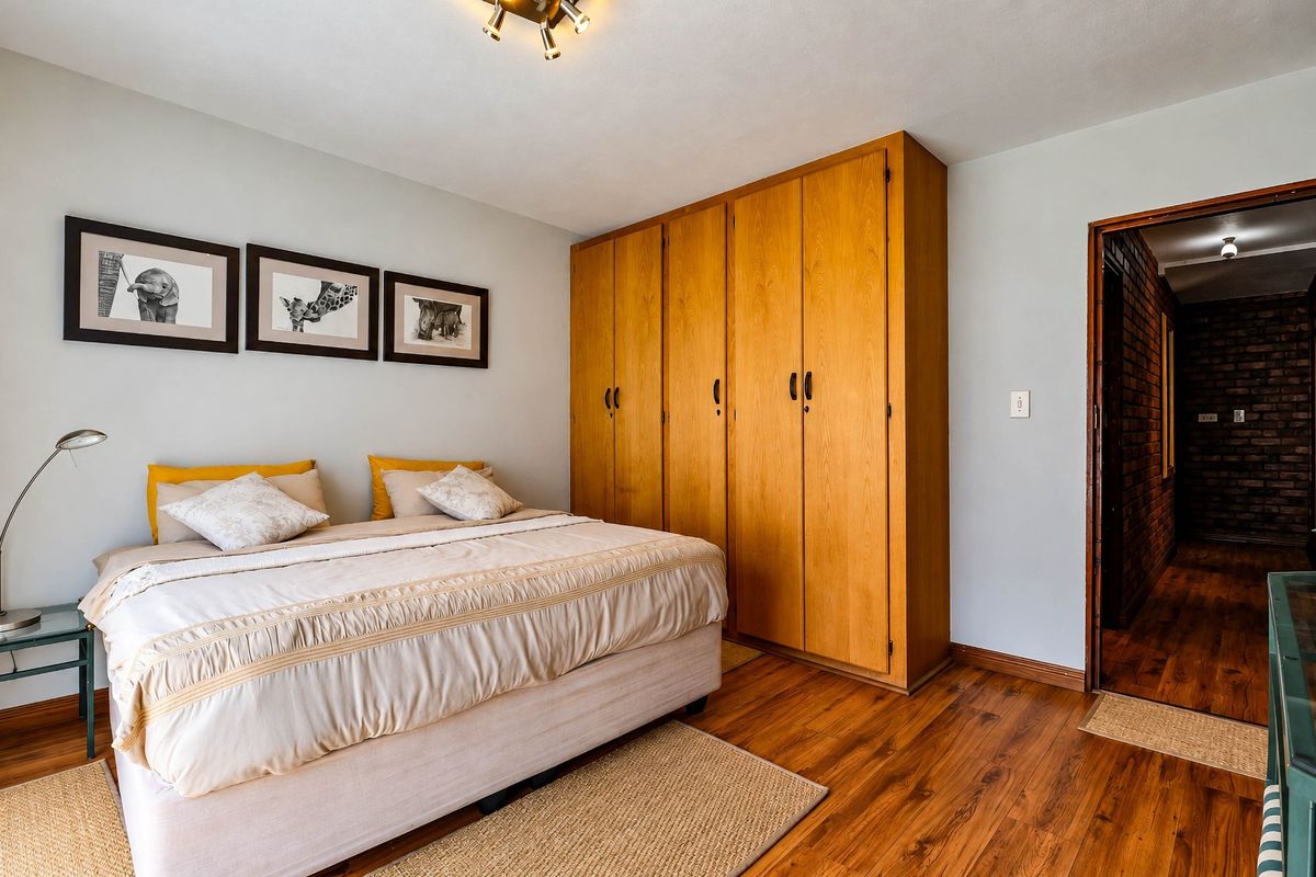 A well-maintained bedroom featuring warm laminate flooring, a large built-in wooden wardrobe, and neutral wall tones.