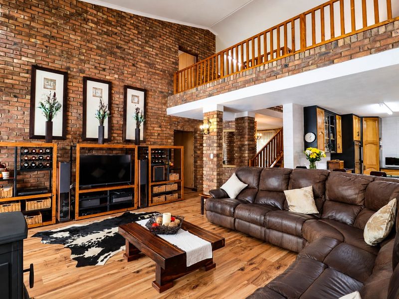 Spacious open-plan living area featuring exposed brick walls, a vaulted ceiling, mezzanine level, and a cozy wood-burning stove with warm laminate flooring.
