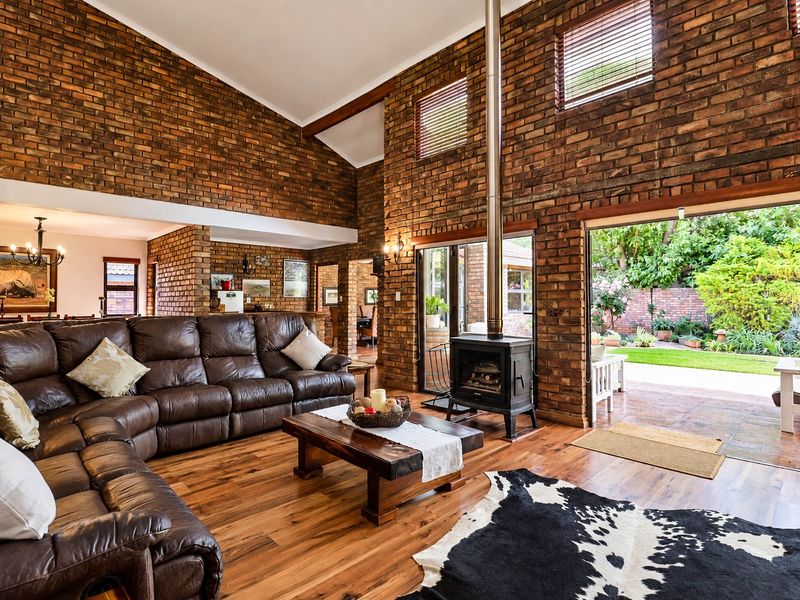 Spacious living room featuring high vaulted ceilings, exposed brick walls, timber flooring, and a wood-burning fireplace, with direct access to the rear garden.
