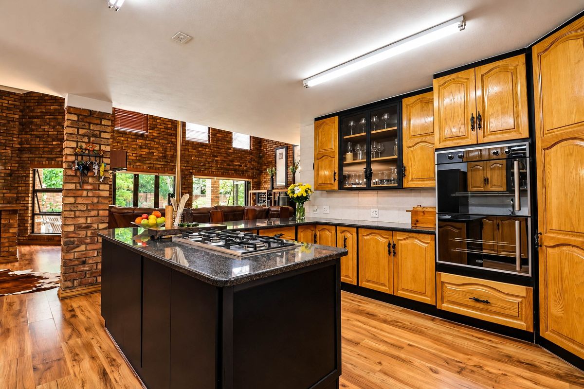 Spacious kitchen featuring a central island with gas hob, built-in oven, granite countertops, and warm timber cabinetry, complemented by an exposed brick feature wall.