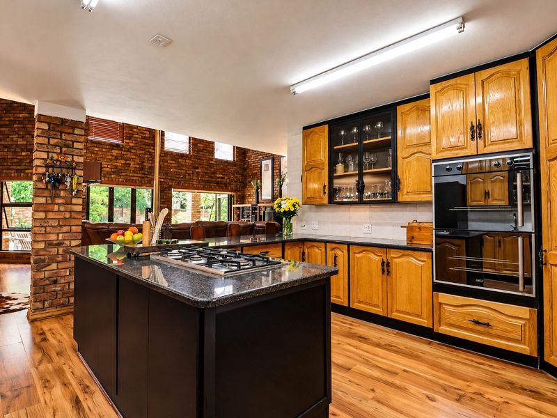 Spacious kitchen featuring a central island with gas hob, built-in oven, granite countertops, and warm timber cabinetry, complemented by an exposed brick feature wall.