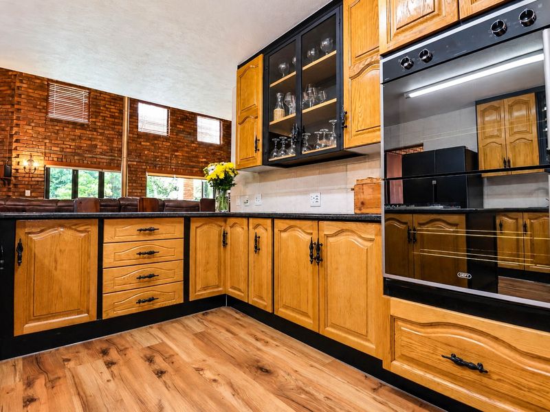 A well-maintained kitchen featuring warm wood cabinetry, granite countertops, a built-in oven, and a striking exposed brick feature wall.