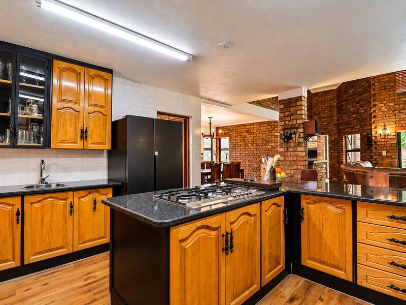 Open plan kitchen featuring wooden cabinetry, granite countertops, and a gas hob, seamlessly flowing into the adjacent living and dining areas with exposed brick accents.