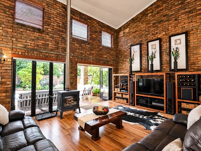 Spacious living room featuring high vaulted ceilings, exposed brick walls, timber flooring, and a central wood-burning fireplace with direct access to the patio.