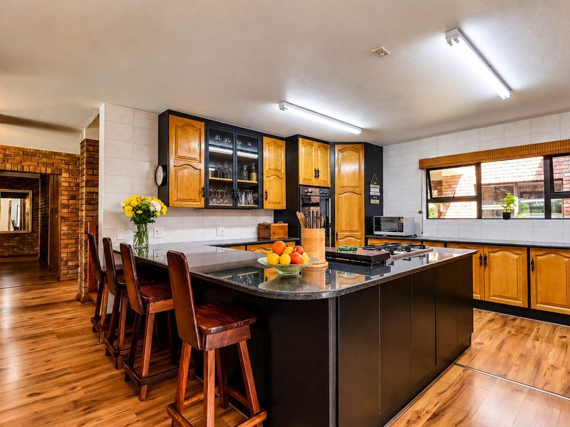 A spacious kitchen featuring dark cabinetry, granite countertops, a central island with a gas hob, and warm laminate flooring with exposed brick accents.