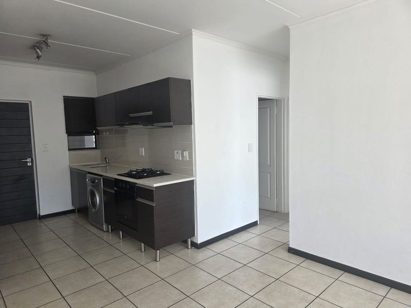 A compact, modern kitchen featuring dark cabinetry, a gas hob, built-in oven, and tiled flooring, offering a clean and functional workspace.