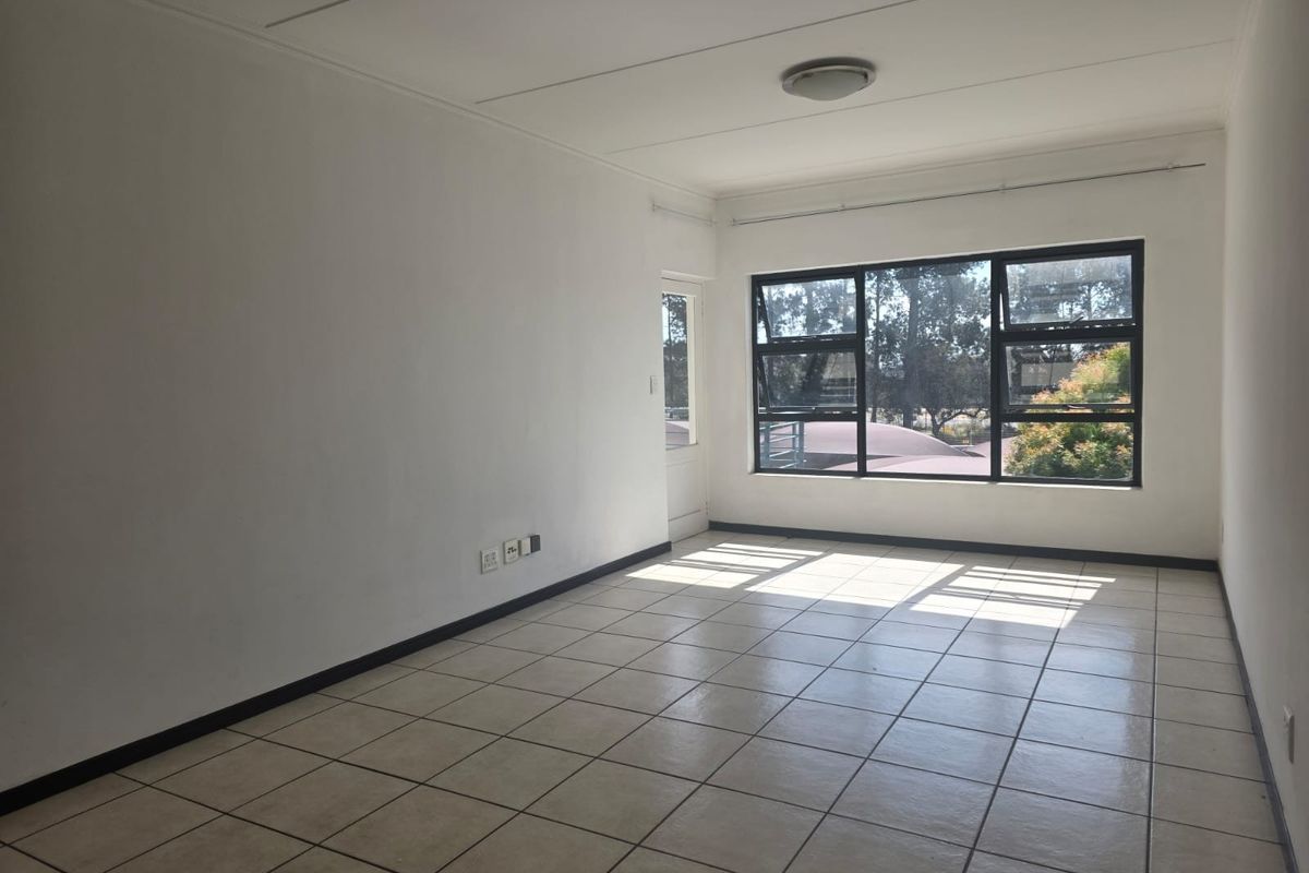 A bright, empty living room featuring neutral tiled flooring, large windows providing natural light, and clean white walls, ready for personalization.