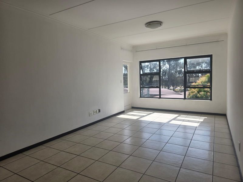 A bright, empty living room featuring neutral tiled flooring, large windows providing natural light, and clean white walls, ready for personalization.