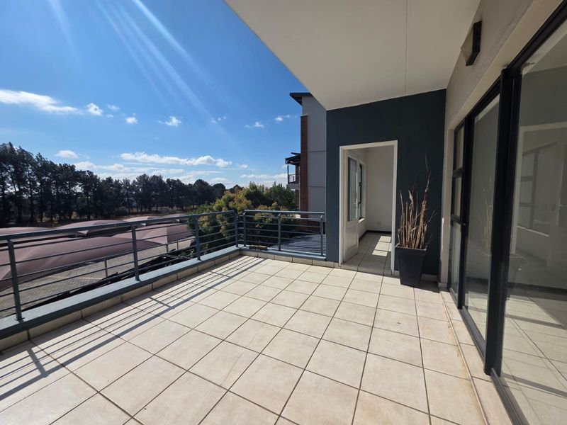 A spacious, covered balcony featuring tiled flooring and a metal balustrade, offering an open outdoor area accessible through sliding glass doors.