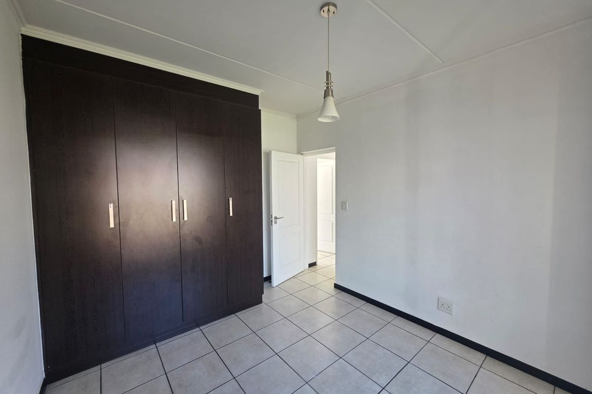 A clean, empty bedroom featuring dark wood built-in cupboards, neutral tiled flooring, and a modern pendant light fixture.