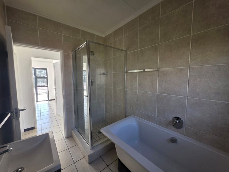 A clean, modern bathroom featuring a separate shower enclosure, a bathtub, and neutral ceramic tiling throughout.