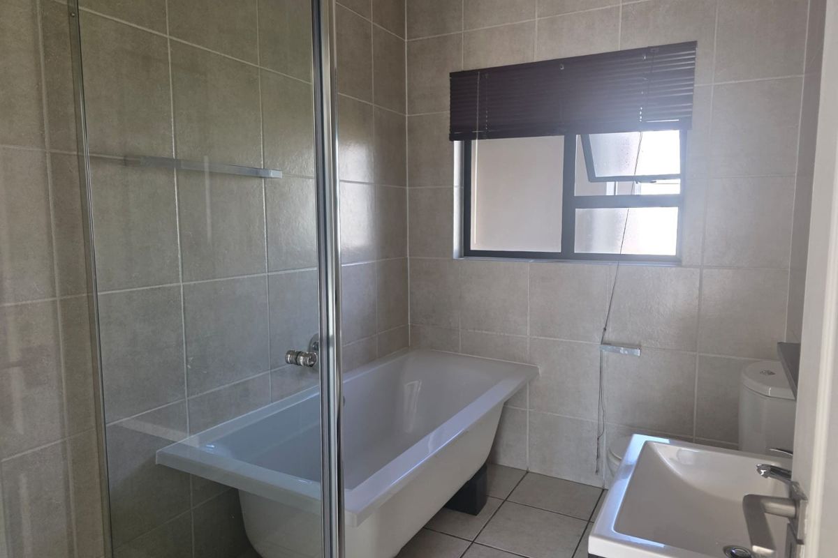 A functional bathroom featuring a glass shower enclosure, a built-in bathtub, a vanity basin, and neutral ceramic tiling throughout.