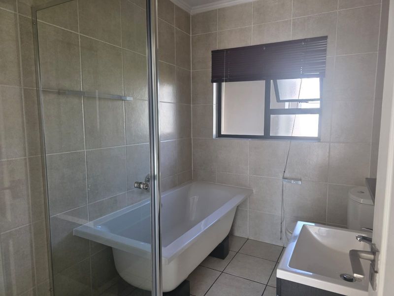 A functional bathroom featuring a glass shower enclosure, a built-in bathtub, a vanity basin, and neutral ceramic tiling throughout.