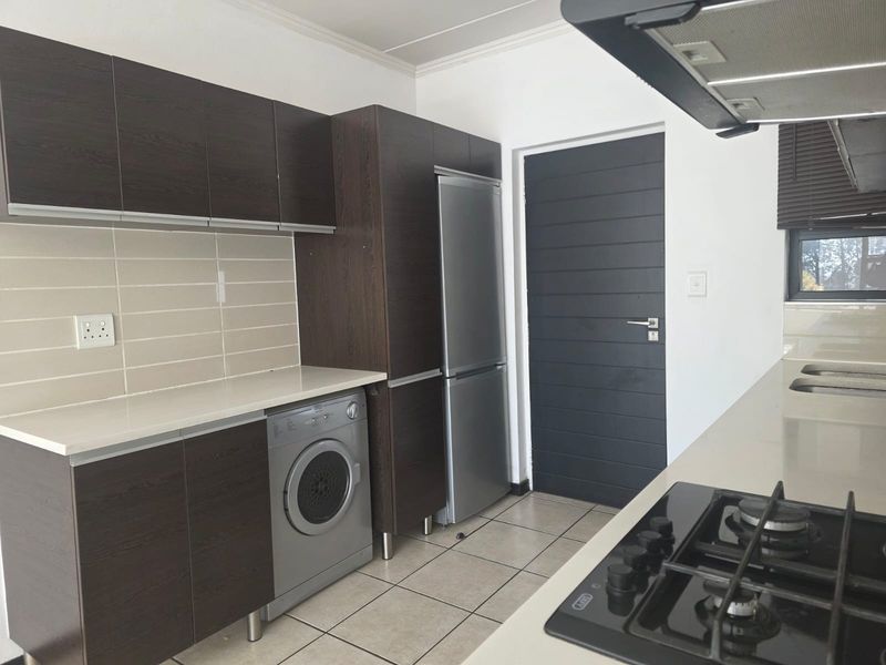 Modern kitchen featuring dark wood cabinetry, stone countertops, tiled backsplash, gas hob, extractor fan, and integrated laundry space with tiled flooring.