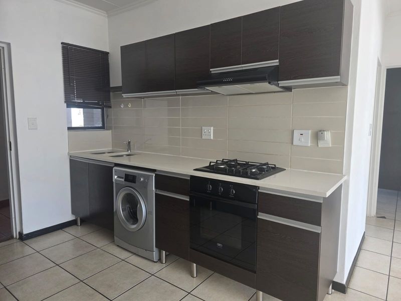 Modern kitchen featuring dark wood cabinetry, built-in oven, gas hob, extractor fan, and tiled backsplash with neutral floor tiles.