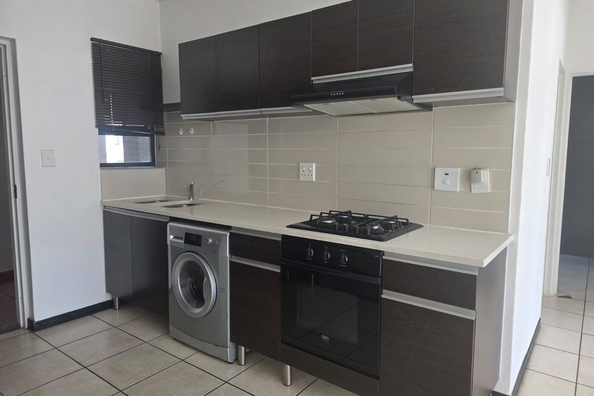 Modern kitchen featuring dark wood cabinetry, built-in oven, gas hob, extractor fan, and tiled backsplash with neutral floor tiles.