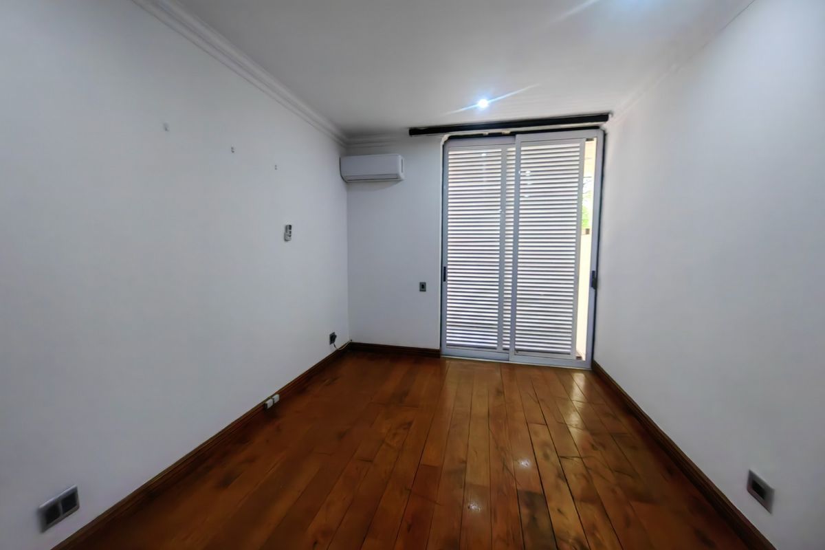 An empty bedroom featuring polished hardwood flooring, a wall-mounted air conditioning unit, and a sliding glass door providing access to the exterior.