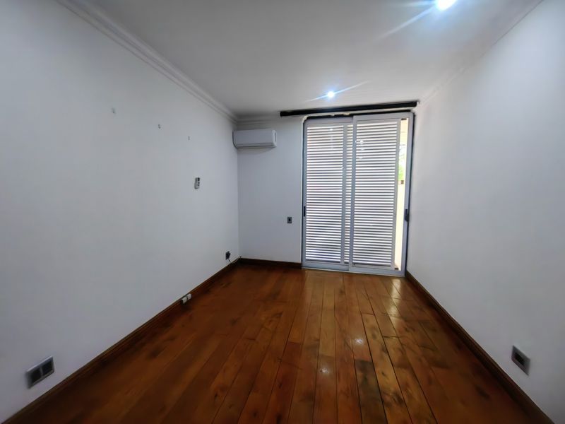 An empty bedroom featuring polished hardwood flooring, a wall-mounted air conditioning unit, and a sliding glass door providing access to the exterior.