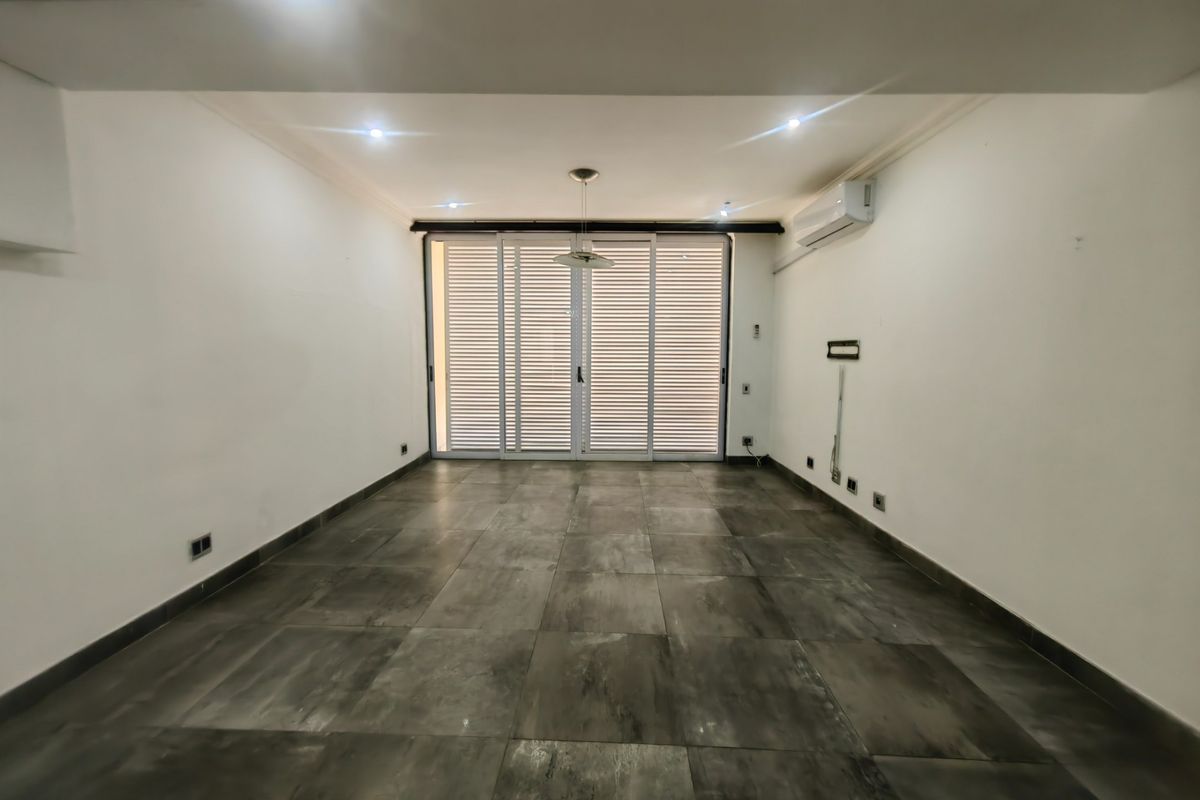 A spacious, empty living area featuring large format floor tiles, recessed lighting, a split-system air conditioner, and sliding glass doors with integrated blinds.