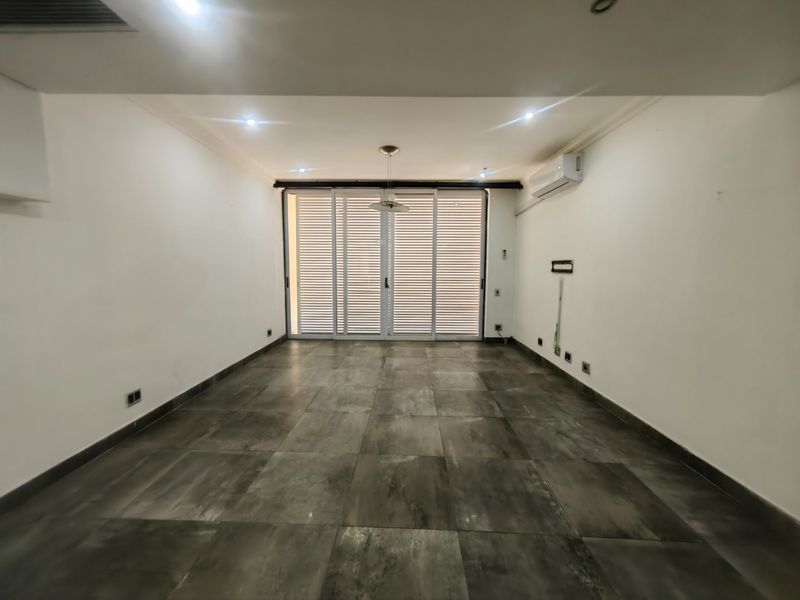 A spacious, empty living area featuring large format floor tiles, recessed lighting, a split-system air conditioner, and sliding glass doors with integrated blinds.