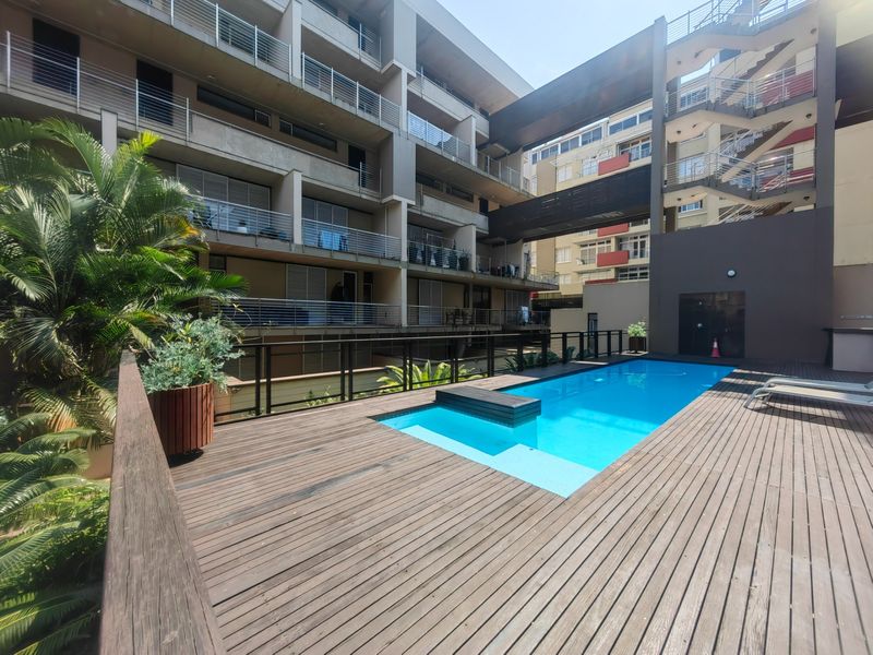 Communal swimming pool area featuring timber decking and modern apartment building architecture with metal balustrades.