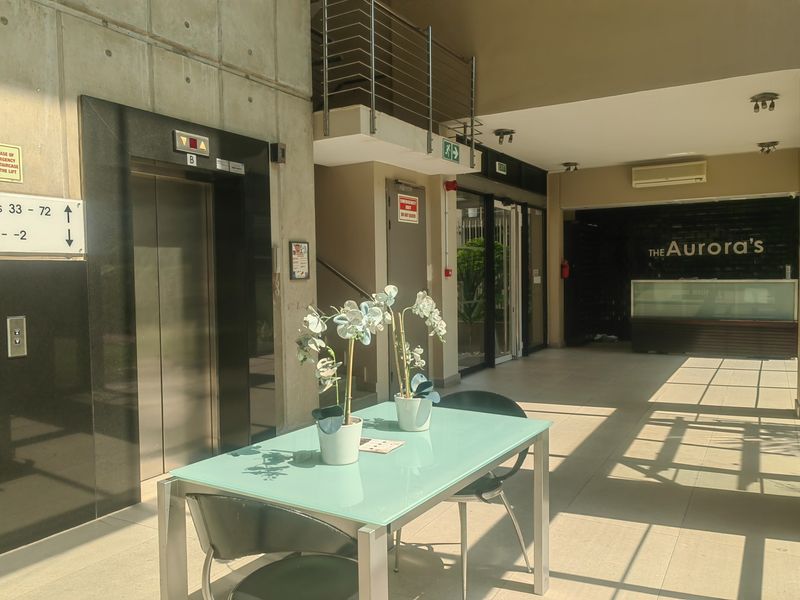 A modern apartment building lobby featuring a reception area, elevator access, and a staircase, finished with clean tiling and contemporary architectural elements.