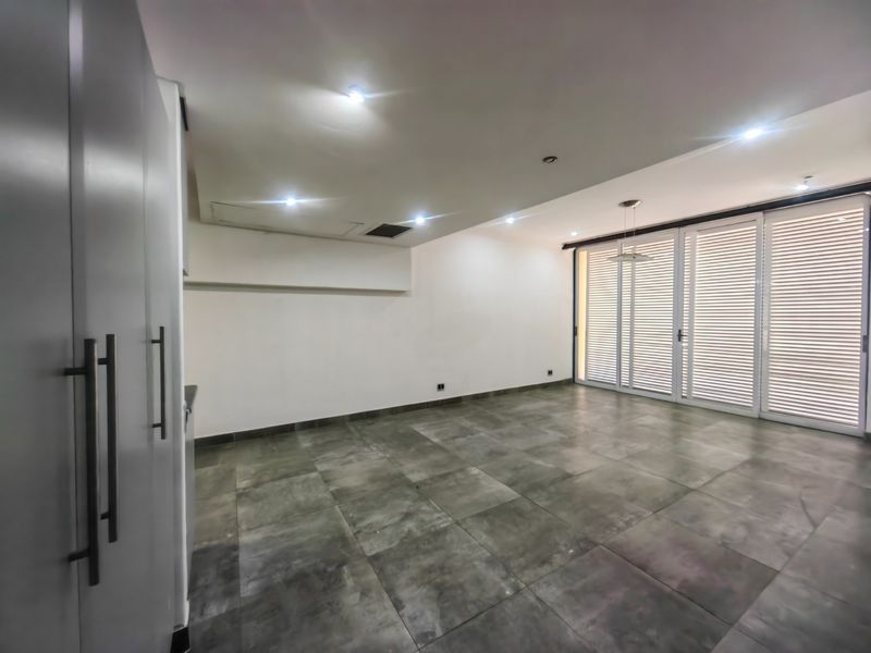 Spacious open-plan living area featuring large format floor tiles, recessed downlighting, built-in cabinetry, and expansive sliding glass doors with integrated louvre shutters.