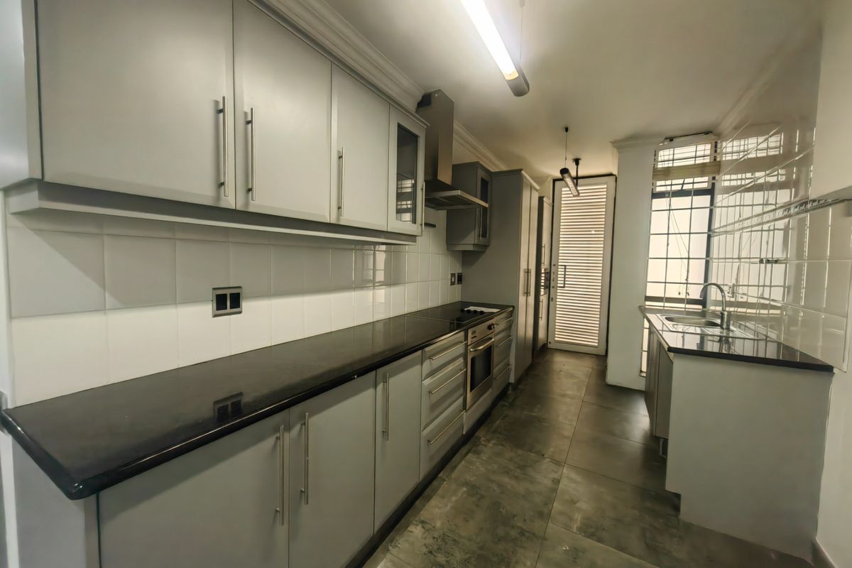 A modern, well-maintained kitchen featuring sleek grey cabinetry, dark granite countertops, built-in oven, extractor fan, and tiled flooring with a secure rear entrance.