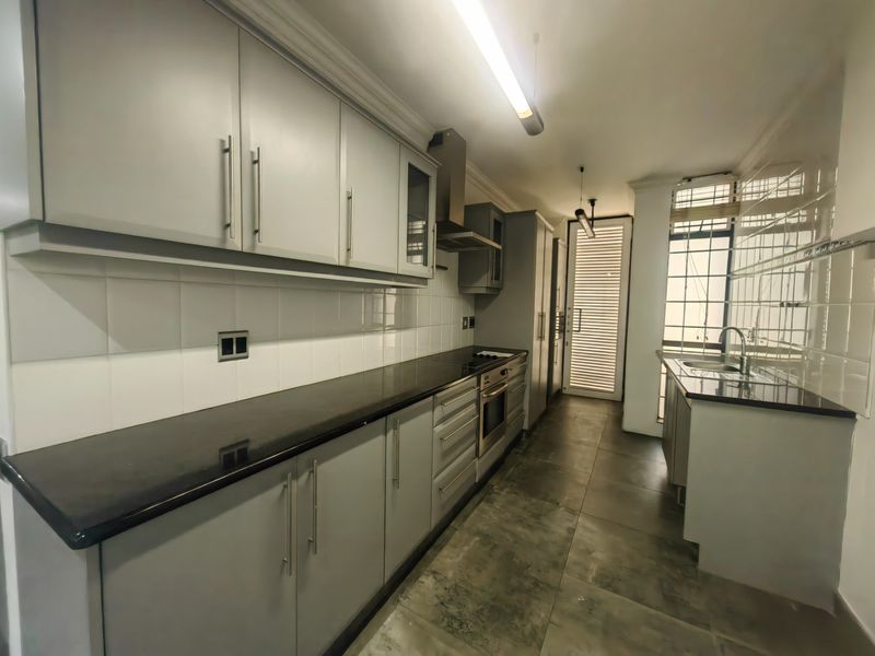 A modern, well-maintained kitchen featuring sleek grey cabinetry, dark granite countertops, built-in oven, extractor fan, and tiled flooring with a secure rear entrance.