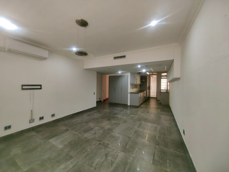 Spacious open-plan living and kitchen area featuring large format floor tiles, modern built-in cabinetry, and integrated air conditioning.