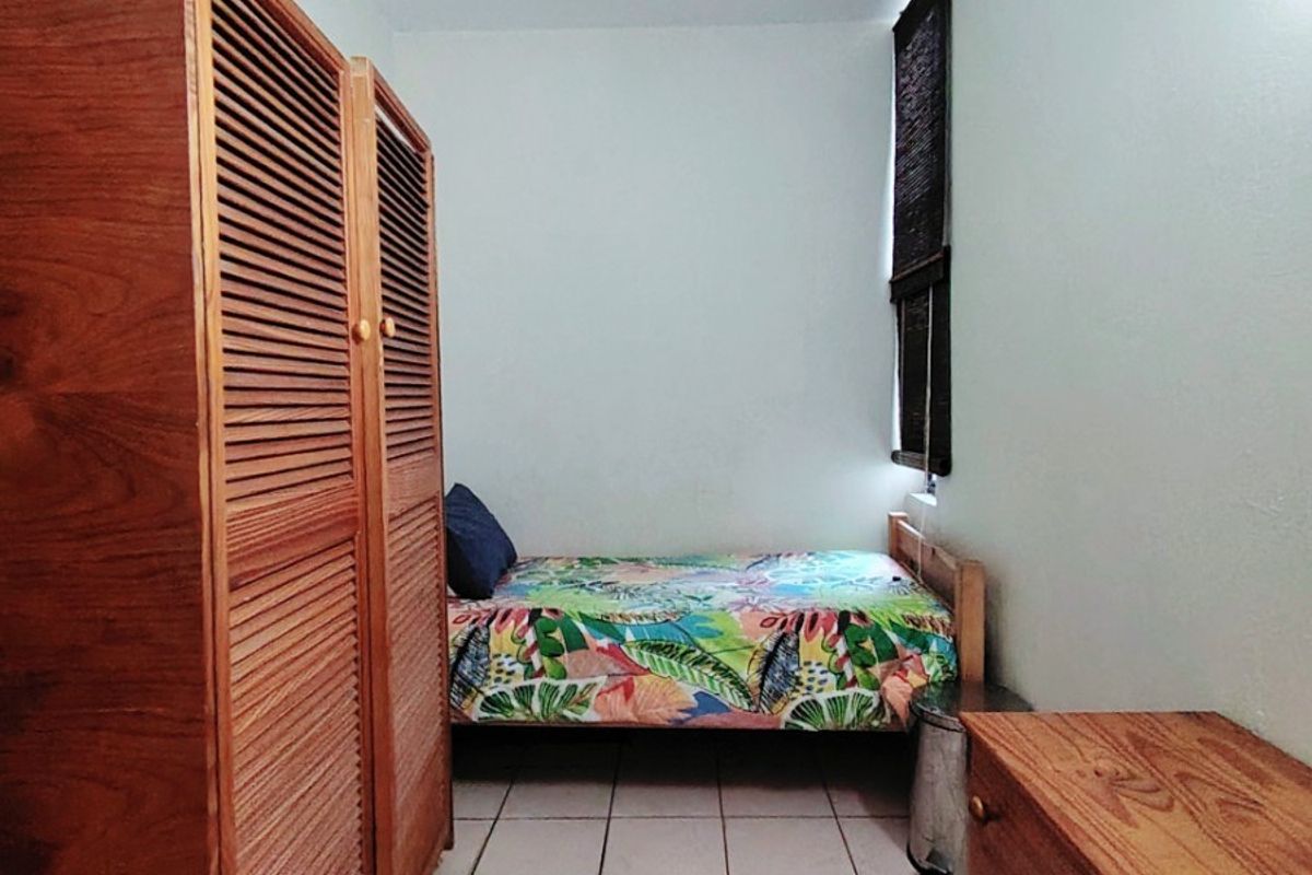 A compact bedroom featuring tiled flooring, a built-in wooden wardrobe, and a window with blinds.