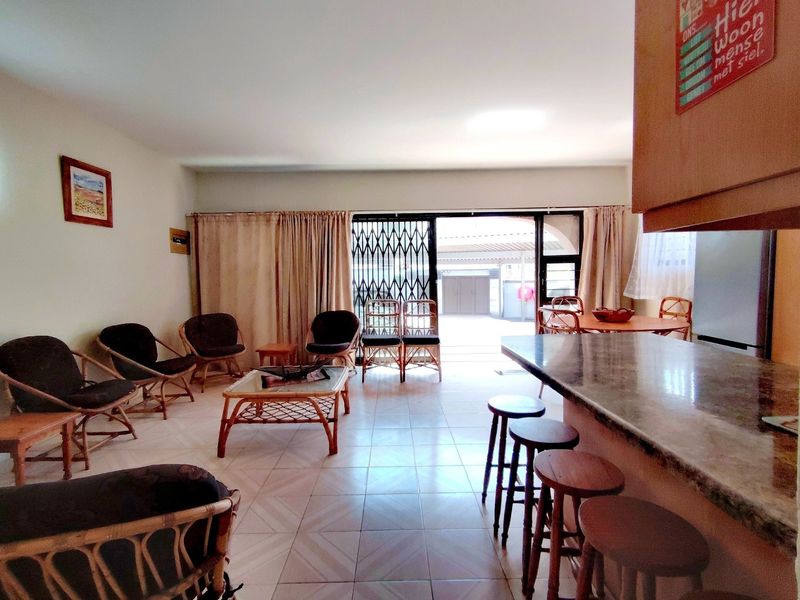 Open-plan living and dining area featuring tiled flooring, a breakfast bar, and a sliding door leading to an outdoor space.
