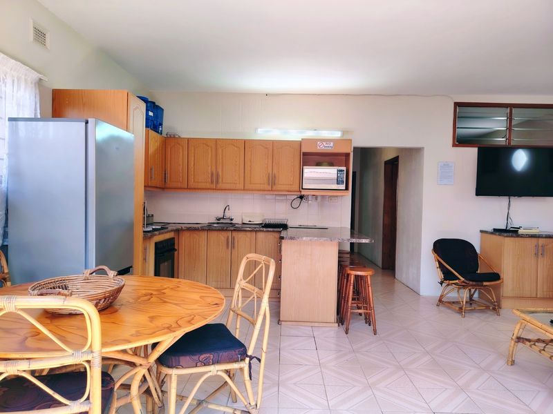 Open plan living and kitchen area featuring wooden cabinetry, tiled flooring, and integrated appliances, offering a functional and connected living space.