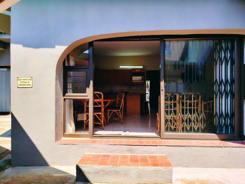 A covered patio entrance featuring a sliding glass door with security gate, leading into an open-plan living and kitchen area.